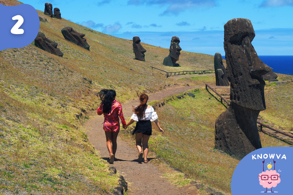 Moai statues on Easter Island standing on grassy hills beside a walking path near the ocean.