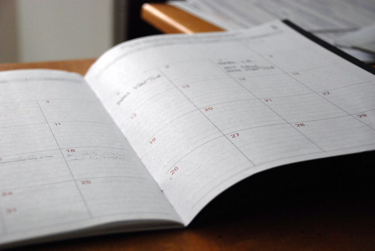 An open paper planner showing a monthly calendar layout with dates and handwritten notes, placed on a wooden desk.