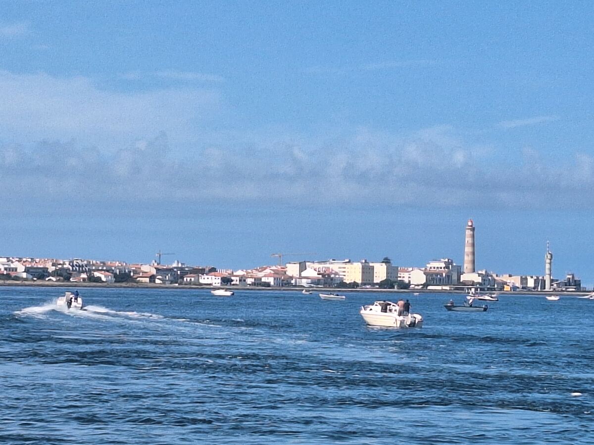 The photo shows eight small fishing boats and the Praia da Barra lighthouse on a summer morning.